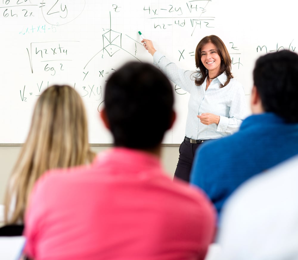 Teacher giving a lecture in a classroom and writing math formulas on the board